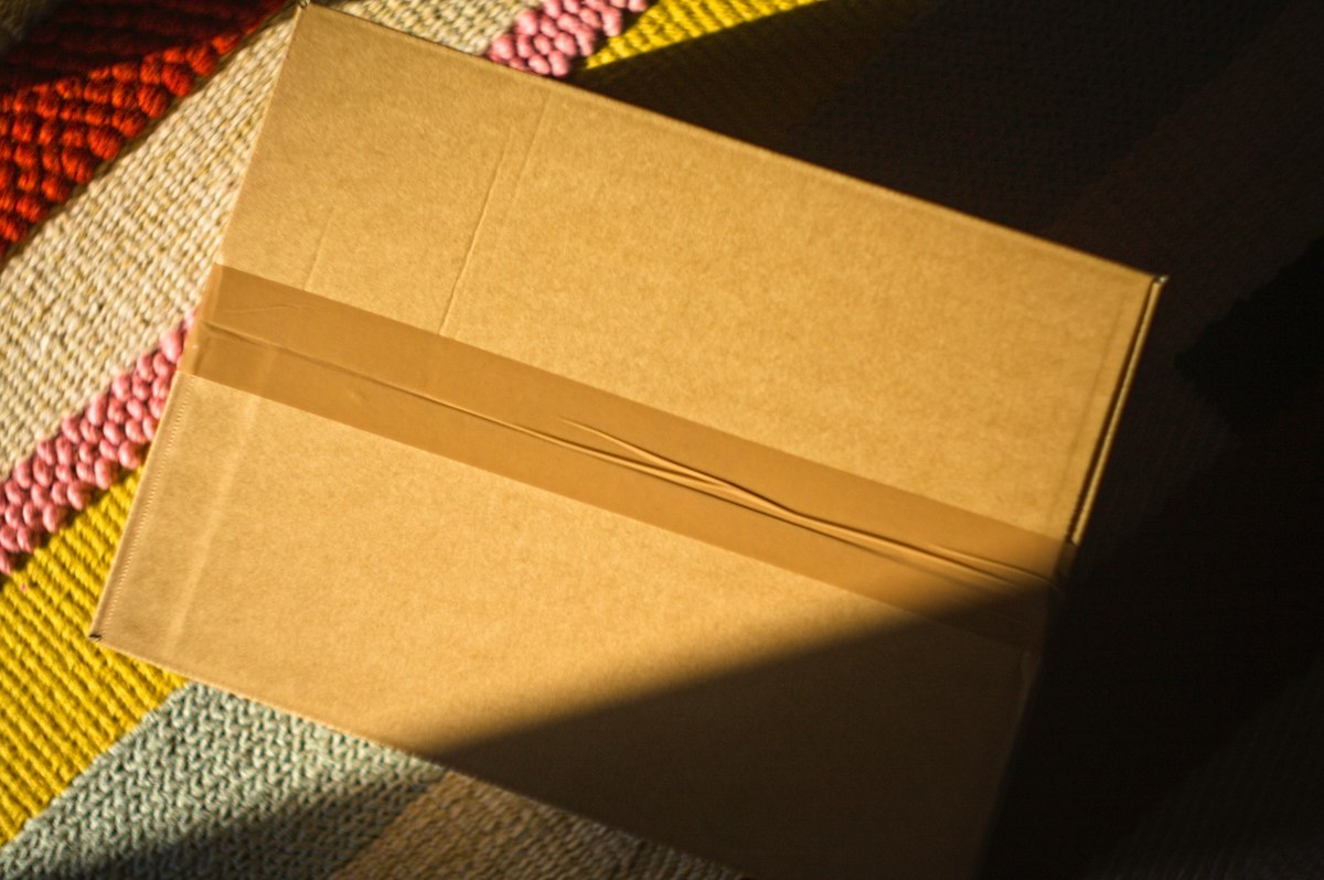 Caixa de papelão sem marca fechada com fita sobre um tapete.