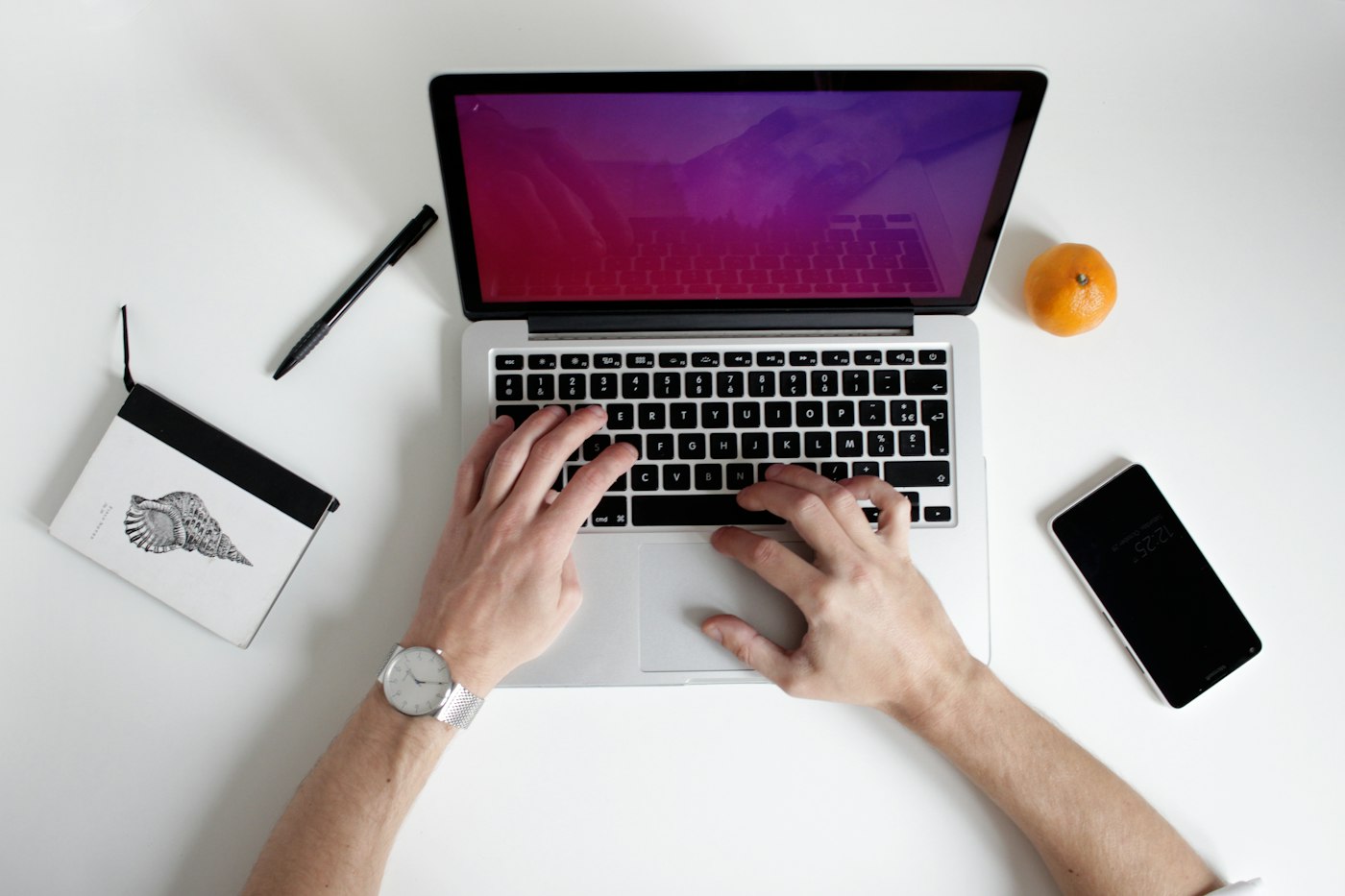 Vista superior de mãos usando um notebook, com um smartphone ao lado.