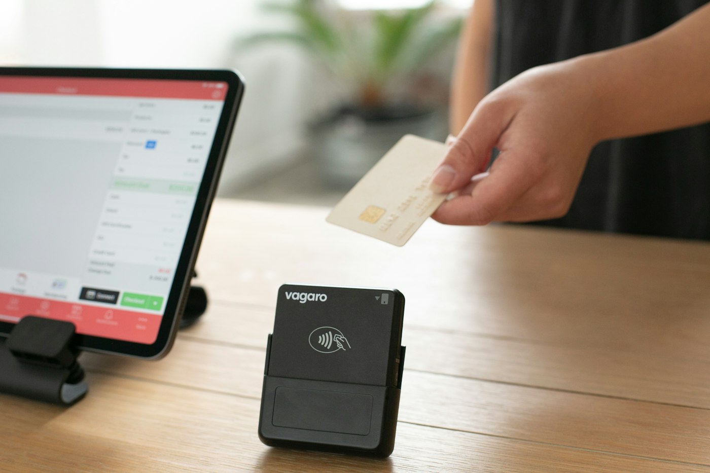 Pessoa aproxima um cartão de um leitor de pagamento sobre uma mesa.